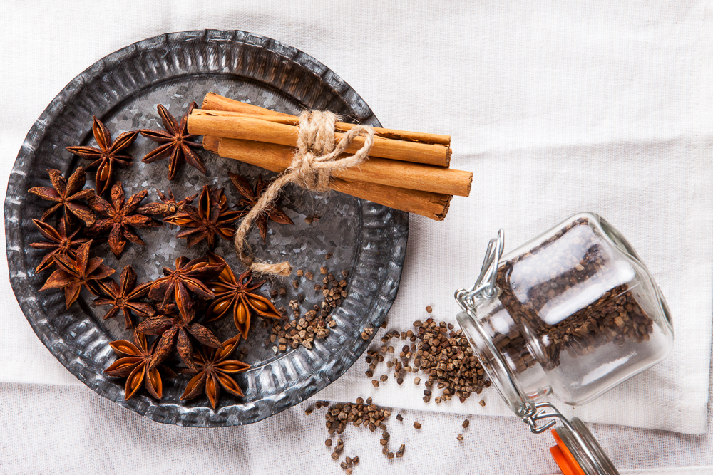 Decorative, sparse christmas arrangement with greeting card copyspace for "Merry Christmas"-text. Cinnamon sticks, star anise and cardamom on white table cloth.