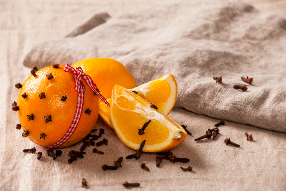 Decorative, sparse christmas arrangement with greeting card copyspace for "Merry Christmas"-text. Orange with clover and ribbon on a brown table cloth. Shallow focus.
